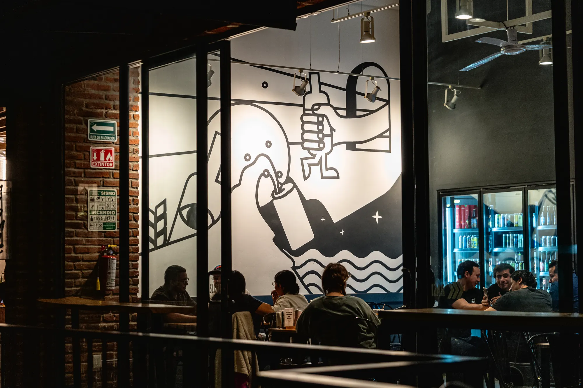 Fachada e interior nocturno de Craft Americana con clientes en la barra